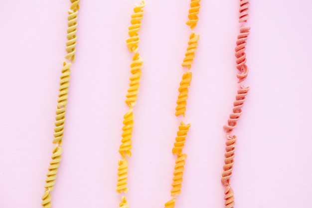 Beautiful Italian uncooked colored farfalle pasta closeup on pink background horizontal top view