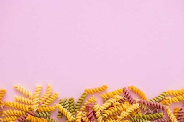 Beautiful Italian uncooked colored farfalle pasta closeup on pink background horizontal top view