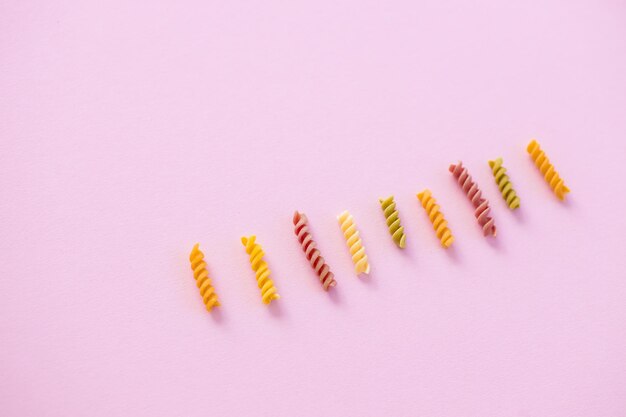 Beautiful Italian uncooked colored farfalle pasta closeup on pink background horizontal top view