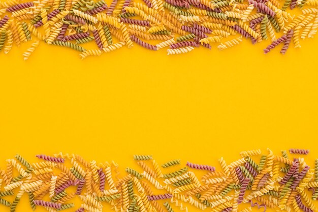 Beautiful Italian uncooked colored farfalle pasta closeup on yellow background horizontal top view