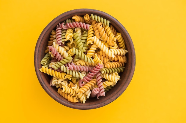 Beautiful Italian uncooked colored farfalle pasta closeup on yellow background horizontal top view