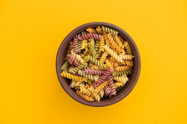 Beautiful Italian uncooked colored farfalle pasta closeup on yellow background horizontal top view