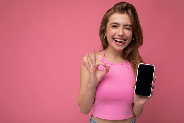 Photo beautiful joyful young blonde woman wearing pink top poising isolated on pink background with empty