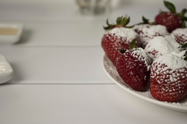 Photo beautiful juicy ripe red strawberries sprinkled with powdered sugar on a white round plate