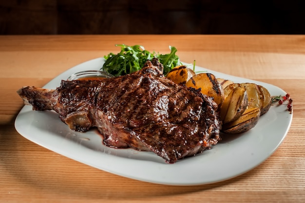 A beautiful juicy steak with salad on  plate is on the wooden table.