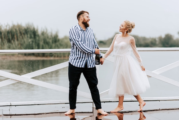 Beautiful just married dance barefoot and have fun on the pier by the water.