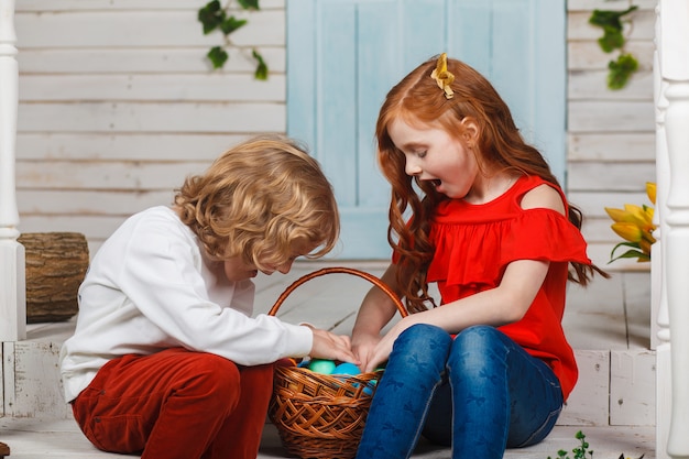 Beautiful kids sit together with a basket of Easter eggs