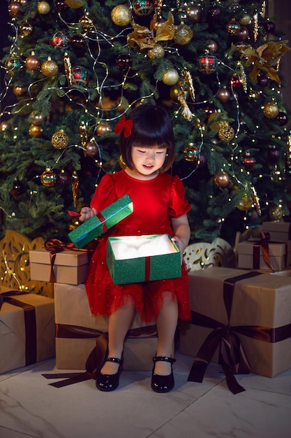 Beautiful Korean girl child in a red dress opens a green gift box .sitting on boxes