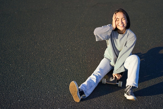 美しい韓国の 10 代の少女はスケート ボードに座っているし、晴れた日の笑顔の若いアジア女性スケートを楽しんでいます