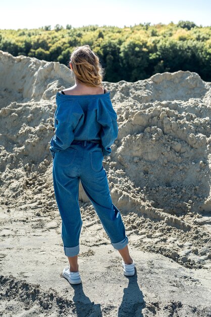 Beautiful lady in blue overalls walks in a sand quarry, active way