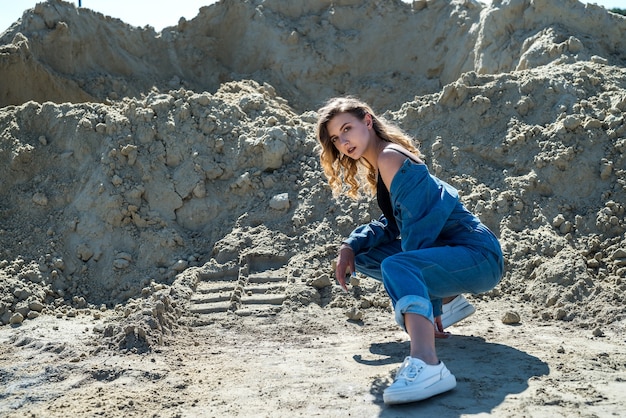 Beautiful lady in blue overalls walks in a sand quarry, active way