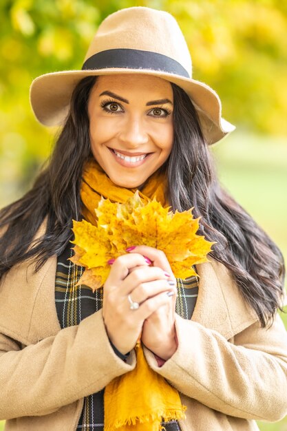 Beautiful lady in fashionable clothes holds yellow maple leaves outdoors.