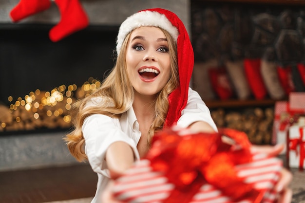 Beautiful lady, long straight hair, red santa hat holding a gift box.