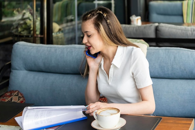 Beautiful lady sitting at the restaurant and talking on the phone while looking at her notes