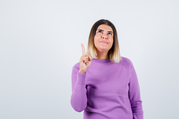 Beautiful lady in sweater pointing up and looking confident , front view.