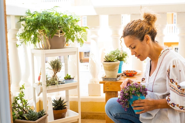 写真 美しい女性はバルコニーで彼女の植物を世話します 座っている金の女性は彼女の花を賞賛します 趣味と植物学的なケアコンセプト