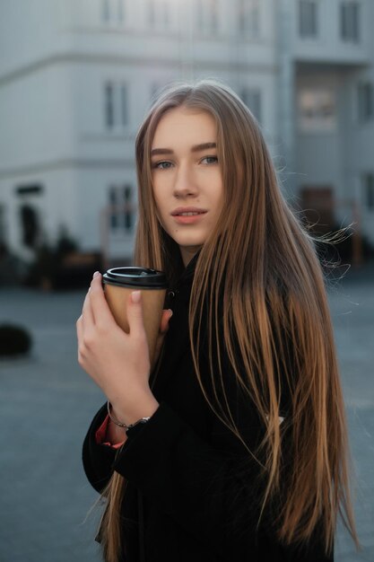 Beautiful lady with long hair with takeaway coffee in the\
street female student for a walk coffee break