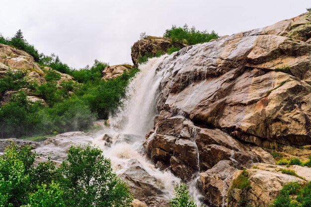 Beautiful landscape of big waterfall in cloudy weather Mountain waterway with green vegetation in summertime