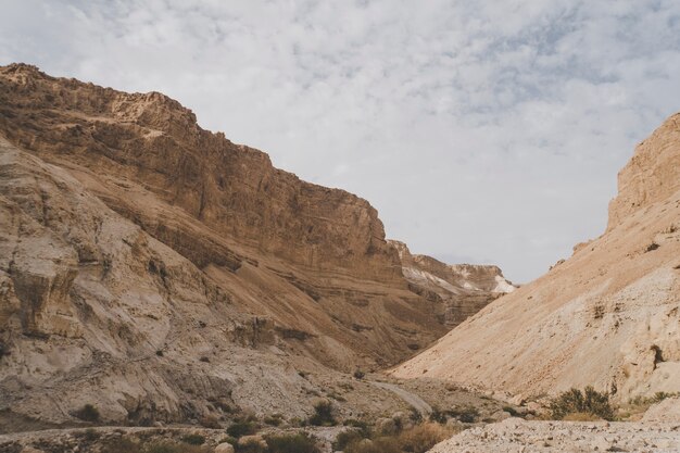 晴れた日に撮ったイスラエルの峡谷の美しい風景。イスラエルのジュダイアン砂漠の曇り空を背景にした山、丘、崖。丘のふもとの貧弱な岩の多い土壌