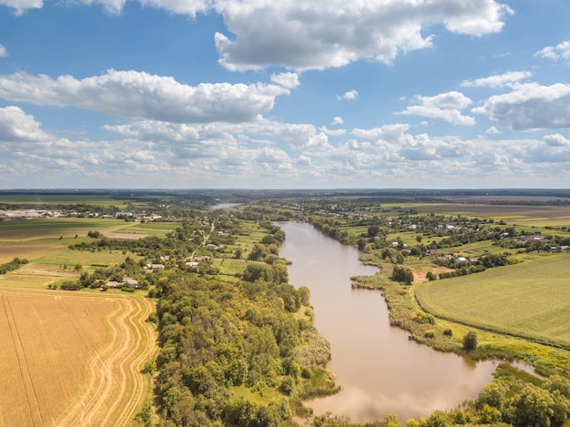 Bellissimo paesaggio con campi agricoli, paese e ampio fiume su uno sfondo di cielo nuvoloso blu in una giornata di sole estivo. vista aerea da drone.
