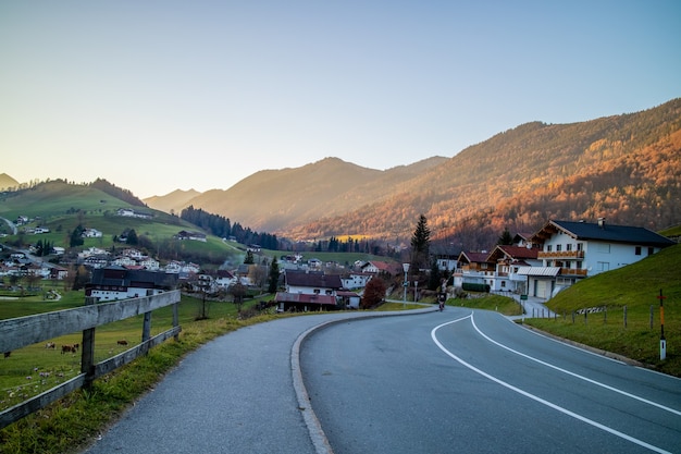Beautiful landscape with asphalt road through the traditional country in Austria on a background of mountains and clear blue sky in a sunny day.