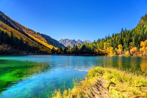 Beautiful landscape with mountain lake and high rocks with illuminated peaks reflection with green water, blue clean sky and yellow autumn sunrise.