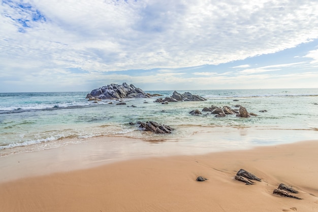 Beautiful lanscape of a sandy beach with rocks in the ocean against a blue sky background.