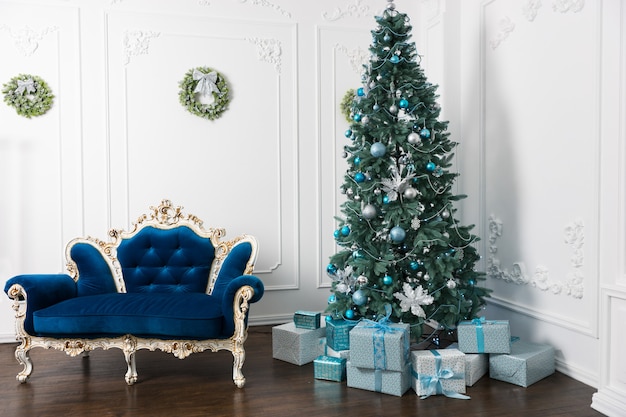 Bellissimo albero di natale grande con tanti regali e diverse decorazioni in camera in stile classico con divano vintage in stile barocco