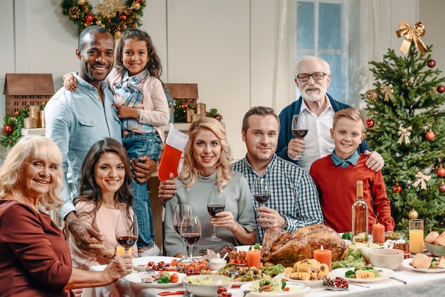 Bella famiglia numerosa che celebra il natale con bicchieri di vino e guardando la fotocamera