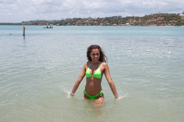 Beautiful Latin American woman in bikini on the beach. Young woman enjoying her summer vacation on a sunny day, smiling and looking at the camera