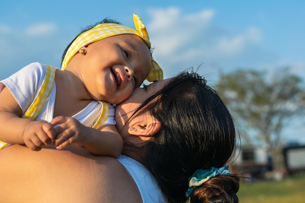 beautiful latin baby girl being held by her mother,  smiling and holding her cheeks together