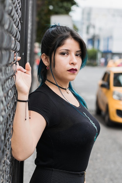 Beautiful latin girl on the street leaning on a wire mesh in a closeup