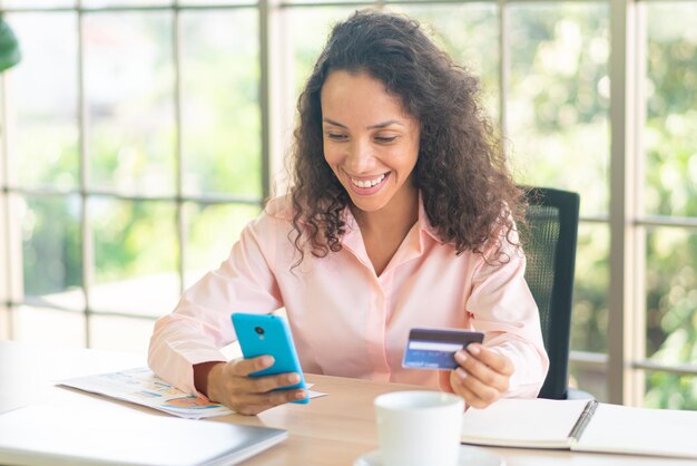 Bella donna latina che utilizza smartphone con la mano che tiene la carta di credito