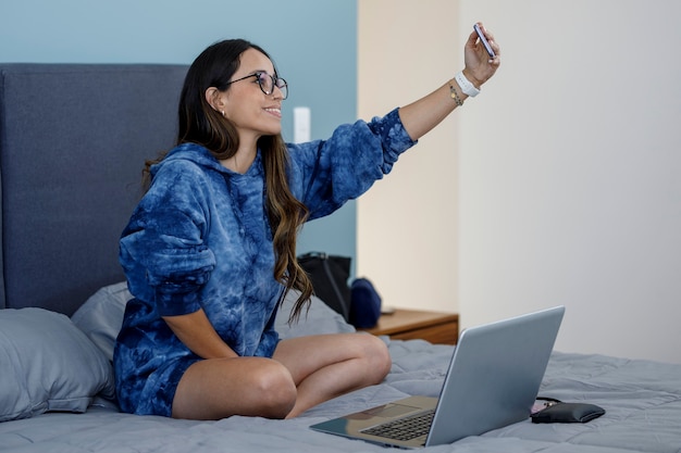 Beautiful latin woman wearing a sweatshirt taking a selfie in her bedroom