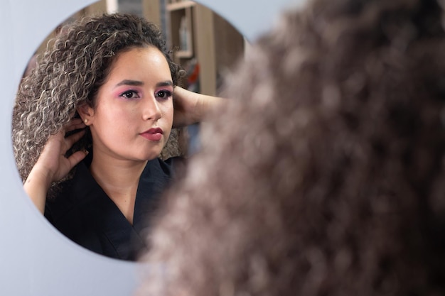 Beautiful latina woman with curly hair flicks her hair in front of the mirror