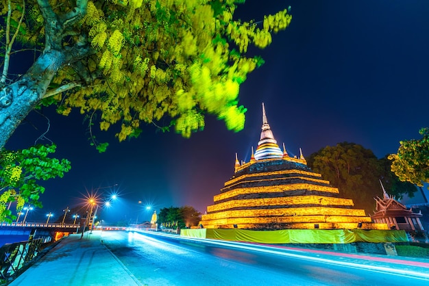 Photo beautiful the lights on the road with yellow flowers cassia fistula at park in phra chedi luang in temple wat ratchaburana is a buddhist temple in phitsanulokthailand at natural twilight