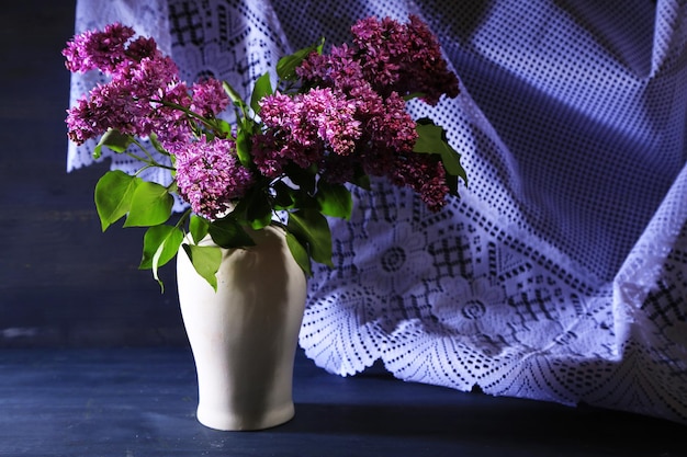 Beautiful lilac flowers in vase on color wooden background