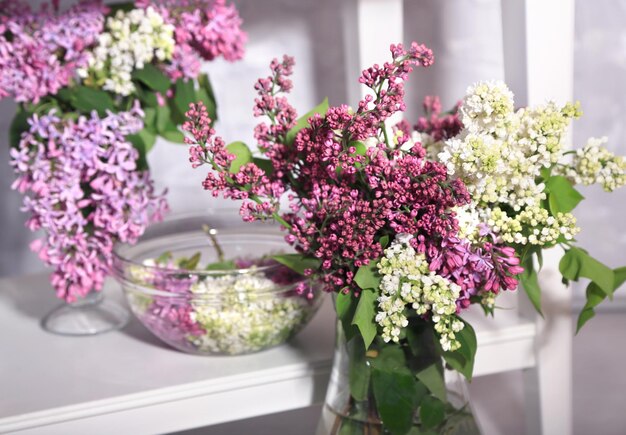 Beautiful lilac flowers in vase on table on light wall background