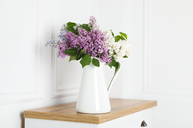 흰 벽 근처의 나무 테이블에 있는 꽃병에 아름다운 라일락 꽃