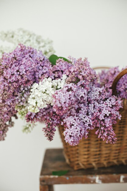 木製の椅子に籐のバスケットに美しいライラックの花 田舎の背景に春の素朴な静物 家庭で紫と白のライラック組成