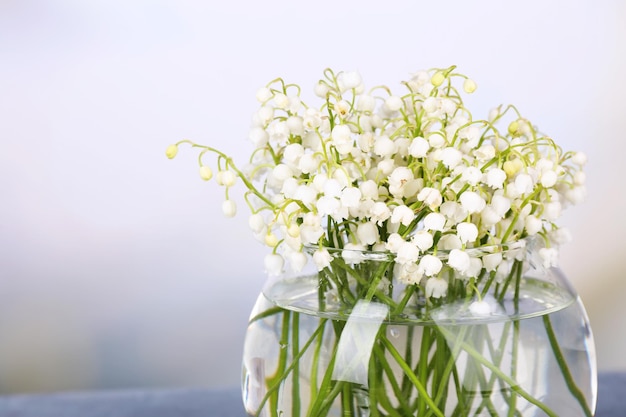 Beautiful lilies of the valley in glass vase on light background