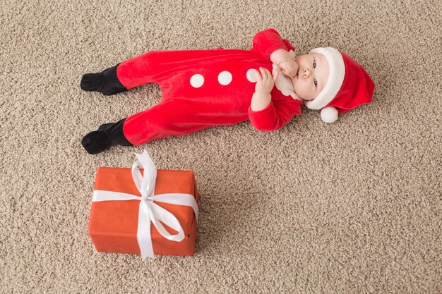 美しい小さな赤ちゃんはクリスマスを祝います。年末年始。クリスマスの衣装とサンタの帽子とギフトボックス、上面図の赤ちゃん。