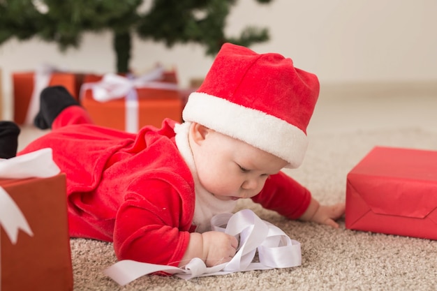 아름다운 작은 아기가 크리스마스를 축하합니다. 설날. 크리스마스 의상과 산타 모자와 선물 상자를 입은 아기.