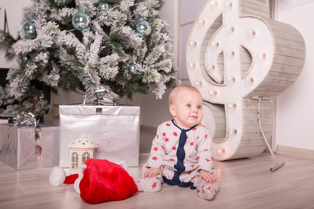 Beautiful little baby celebrates Christmas. New Year&#39;s holidays. Baby in a Christmas costume with gift