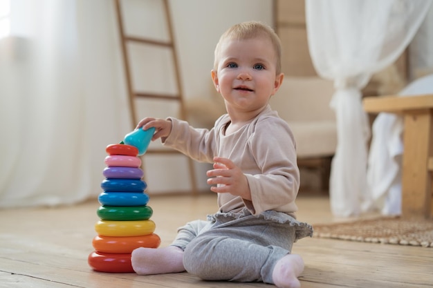 beautiful little baby child playing pyramid game sitting on floor in living room looking away
