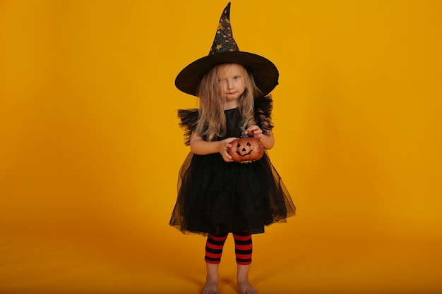 beautiful little blonde girl in a black dress and a witch hat halloween