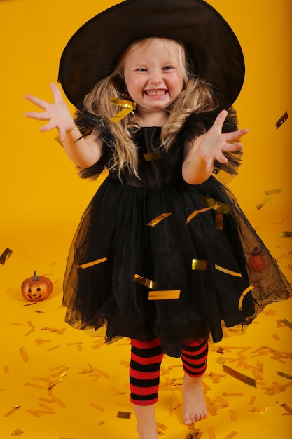 Beautiful little blonde girl in a black dress and a witch hat halloween