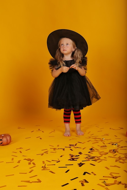 Photo beautiful little blonde girl in a black dress and a witch hat halloween