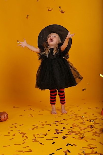 beautiful little blonde girl in a black dress and a witch hat halloween