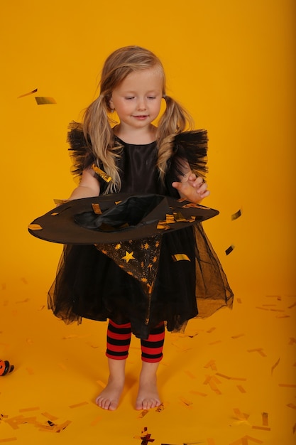 Beautiful little blonde girl in a black dress and a witch hat halloween